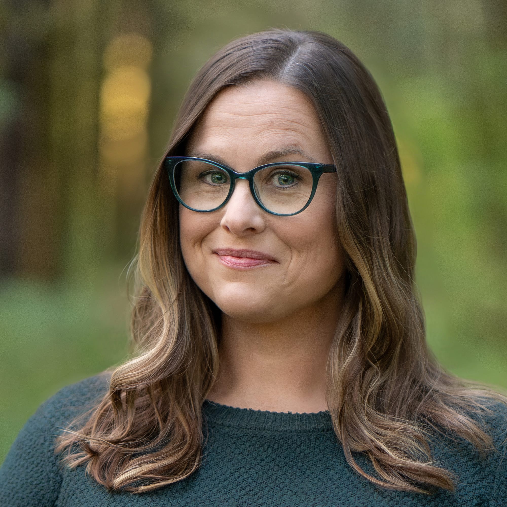 Sarah is a woman with light skin, long brown hair with highlights, and green-framed glasses. 